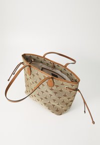 Beige kangaskassi, jossa ruskea abstrakti kuvio, ruskeat nahkayksityiskohdat, kaksi kahvaa ja kiristysnyöri. Sisätasku näkyvissä.