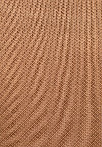 Zacht, strukturiert breiig materiaal in een warme, gedempte oranje tint, met een consistent patroon van in elkaar grijpende steken.