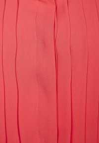 Tessuto plissettato in corallo con pieghe verticali, texture liscia e dettagli di cucitura visibili, adatto per capi d'abbigliamento o decorazioni per la casa.