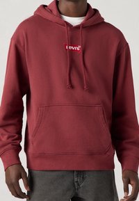 Bordeauxfarbener Hoodie mit Kordelzug, Kängurutasche und gesticktem Levi's-Logo in Rot. Weicher, strukturierter Stoff mit gerippten Bündchen und Saum.