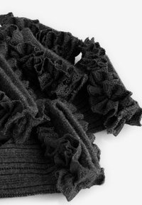 Schwarzes Strickkleidungsstück mit gewellten Säumen, das ein strukturiertes Muster und weichen Stoff aufweist. Das Design umfasst gerippte Abschnitte und filigrane Details.