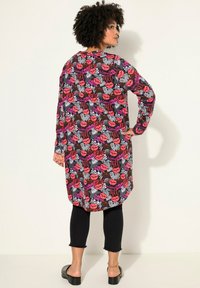 Camicia lunga nera con un vivace motivo di labbra in rosa, rosso e bianco e testo. Maniche lunghe, orlo curvo, abbinata a pantaloni cropped neri e sandali.