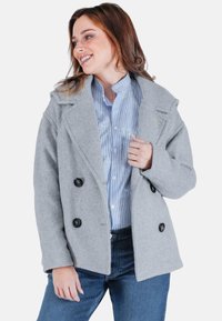 Grau wollener Blazer mit einem doppelt geknöpften Design, vier schwarzen Knöpfen, schmalen Revers und lässigem Schnitt, kombiniert mit einem blauen gestreiften Hemd darunter.