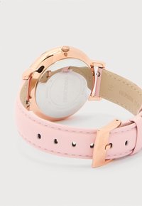 Ροζ χρυσό ρολόι χειρός με λουράκι από αληθινό δέρμα σε ανοιχτό ροζ, ανοξείδωτο ατσάλι πίσω μέρος με χαραγμένο το λογότυπο και τις λεπτομέρειες της Swarovski.