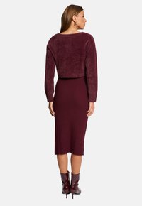 Burgunderfarvet cropped sweater i blødt, fuzzy materiale parret med en ribbet midikjole i samme farve; afsluttet med glinsende burgunderfarvede ankelsko.