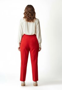 Rote, maßgeschneiderte Hose mit glatter Textur und vorderen Bügelfalten, kombiniert mit einer weißen Bluse mit geknöpften Manschetten, von hinten gesehen.