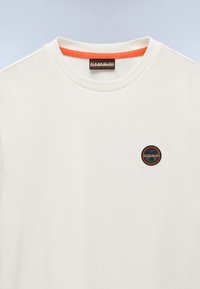T-shirt in cotone bianco con scollo rotondo, caratterizzato da un accento arancione all'interno del colletto e una toppa circolare con logo sul petto.