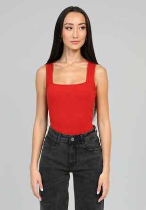 Débardeur rouge côtelé avec un décolleté carré et des bretelles larges, associé à un jean noir en denim taille haute. Détail de logo subtil au niveau de la poitrine.