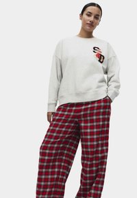 Světle šedá mikina s logem, spárovaná s volnými červenými kostkovanými kalhotami s bílými a modrými pruhy. Pohodlný, neformální design outfitu.