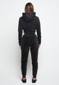 Schwarzer Cord-Trainingsanzug mit einer kurz geschnittenen Kapuzenjacke und passenden, zulaufenden Hosen mit elastischem Bund und Bündchen an den Knöcheln.