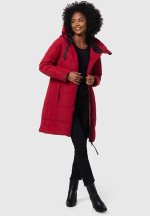 Red padded coat with a hood, featuring black accents, zippered pockets, and a mid-length design, worn over black clothing and ankle boots.