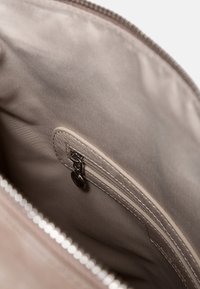 Beżowa torba z zamkiem błyskawicznym w środku z gładkim wykończeniem tkaniny. Zawiera małą kieszonkę na zamek i delikatne szwy wzdłuż krawędzi.