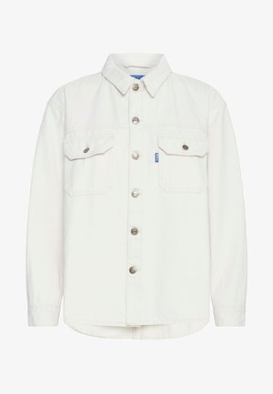 Kermanvärinen farkkupaita, jossa on nappikiinnitys, kaksi rintataskua ja pitkät hihat. Varustettu hopeanvärisillä napeilla ja pyöristetyllä helman muotoilulla.