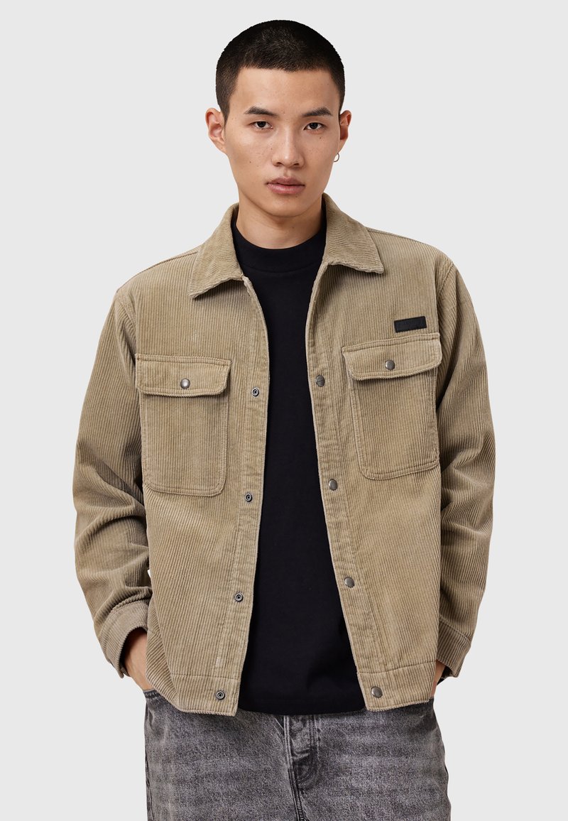 Cordflanellskjorta i beige med två framfickor, tryckknappar, krage och ribbad textur, lager på en svart skjorta.