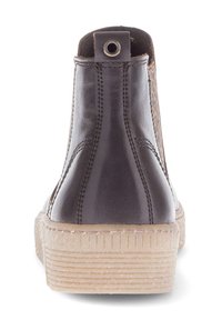 Donkerbruine leren enkellaars met dikke beige, gestructureerde zool, zichtbare stiksels en een trekband met metalen oogje bij de hak.