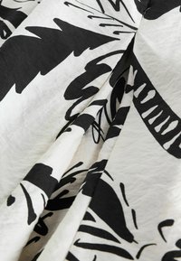 Čierna a biela tkanina s výrazným, abstraktným vzorom listov a textúrovaným povrchom, prehodená tak, aby ukázala záhyby a vrásky.