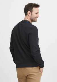 Maglione lungo a maniche corte di colore blu scuro con un motivo testurizzato e polsini a coste, abbinato a pantaloni chinos marrone chiaro, mostrato da dietro.