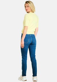 Jasnożółty sweter z krótkim rękawem połączony z niebieskimi dżinsami o slim fit i białymi sneakersami. Cechy obejmują tylne kieszenie oraz miękką teksturę.