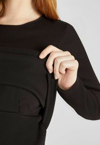 Fekete bordázott top, amely testhez simuló dizájnnal rendelkezik. Az anyag simának és rugalmasnak tűnik, rétegezett részekkel és lekerekített nyakkivágással.