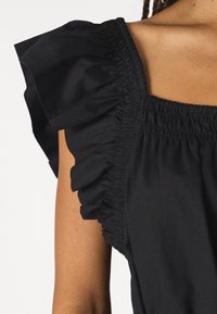 Crop top negru cu decolteu pătrat, detalii cu elastic strâns și mâneci scurte volane. Fabricat dintr-un material ușor.