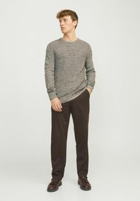 Grijze gebreide trui met een ronde hals, gecombineerd met donkerbruine rechte broek. De outfit heeft een gestructureerde stof en een Relaxed fit.