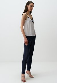 Witte cami-top met marineblauwe rand, rechtvallende marineblauwe broek en zilveren haksandalen. Soepele stof en minimalistisch ontwerp.