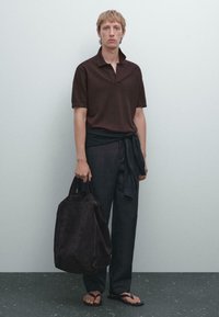 Mørkebrun polo t-shirt, afslappede navy bukser med knyttet talje, sorte sandaler og en mørk ruskinds taske. Simpelt, moderne design.