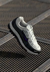 Weißer Sneaker mit schwarzen und lila Akzenten, Obermaterial aus Mesh und Synthetik, strukturierte Sohle und Schnürdesign. Mit Logo an der Seite.