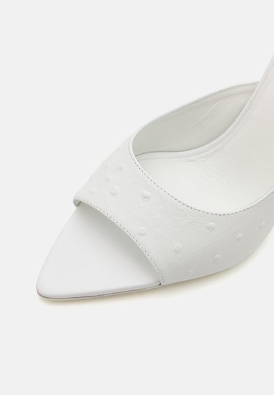 Zapato de tacón blanco de piel con puntera puntiaguda, con una correa texturizada con puntos en relieve. Interior suave, diseño minimalista.
