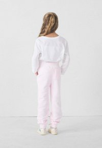 Witte blouse met lange mouwen, roze fleecetrainingsbroek, relaxte pasvorm, elastische boorden, enkele achterzak, gecombineerd met lichtgekleurde sneakers.