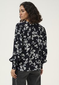 Blusa floreale blu navy con fiori bianchi, con maniche lunghe a sbuffo e polsi arricciati. Tessuto morbido e vestibilità rilassata.