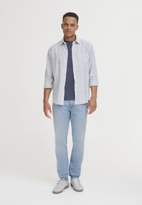Cămașă cu nasturi, în dungi albastre și albe, tricou bleumarin dedesubt, blugi ușor albaștri și adidași gri. Look casual cu mânecile suflecate.