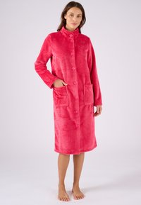 Accappatoio rosa in peluche con superficie texture, colletto alla mandarina, bottoni frontali e due tasche a toppa. Design lungo fino al ginocchio con maniche lunghe.