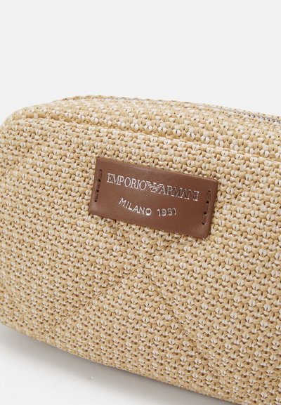Geflochtene Kosmetiktasche aus Stroh in Beige, mit einem braunen Lederetikett und silberner Prägung. Strukturierte Oberfläche mit geometrischem Muster.