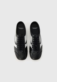 Baskets noir et blanc avec une tige en cuir lisse, présentant un laçage traditionnel, un bout arrondi et un design à rayures contrastées.