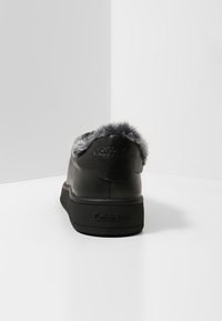 Baskets noires avec bordure en fausse fourrure et logo au talon. Tige en cuir lisse, semelle en caoutchouc texturée, design profilé bas et style minimaliste.