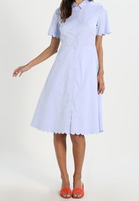 Ljusblå skjortklänning med korta vågformade ärmar, en figurnära bodice och en utrullad kjol som slutar strax under knäet. Vågformad nederdel.