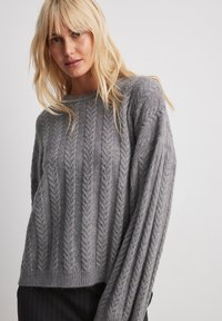 Gray knitted sweater with a ribbed texture and herringbone pattern; features a crew neckline and long sleeves, loose fit.