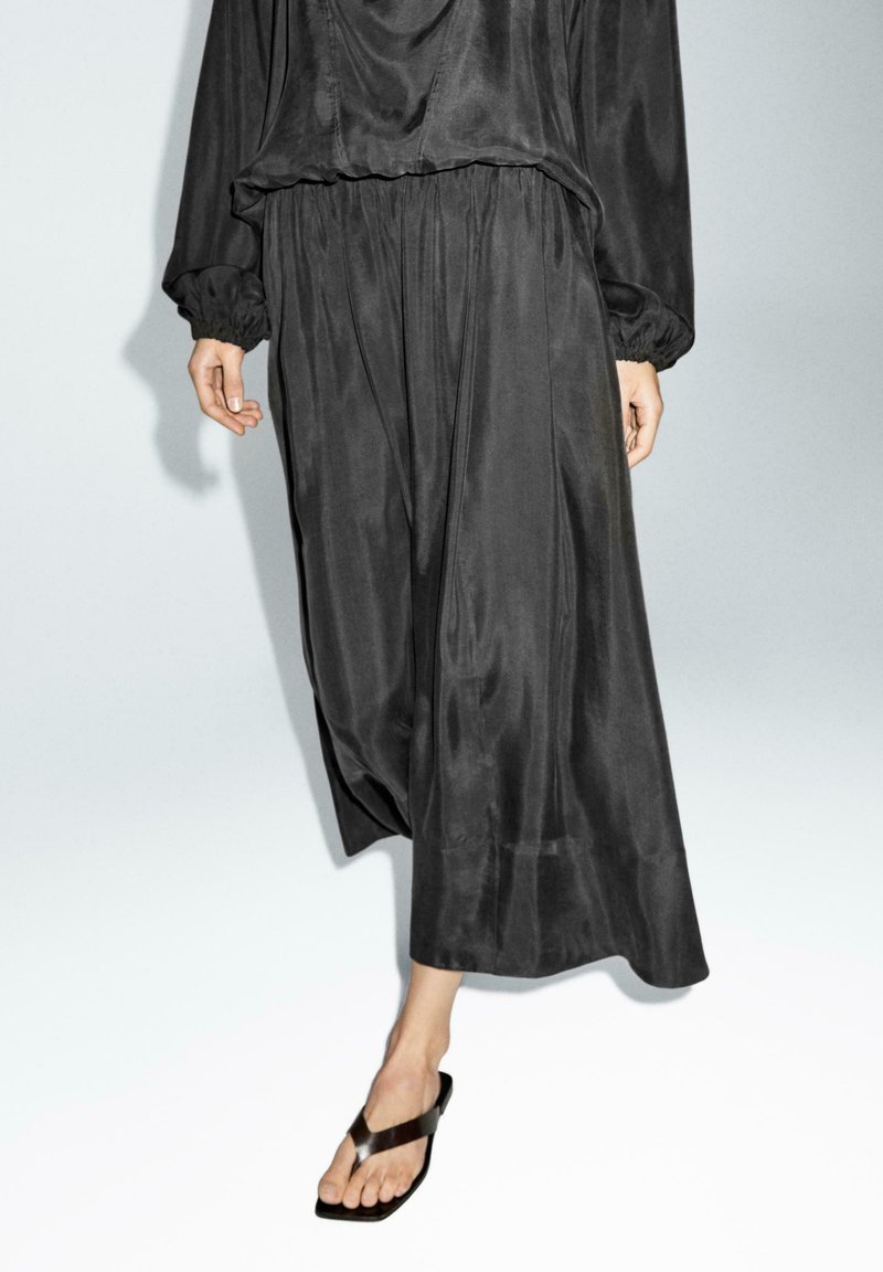 Pantalons larges noirs plissés avec une coupe décontractée, fabriqués en tissu lisse, dotés d'une taille élastique et de poignets froncés.