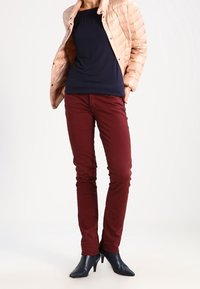 Beżowa kurtka z wypełnieniem, granatowa bluzka i dopasowane burgundowe spodnie. Wysokie granatowe botki dopełniają strój, charakteryzując się gładką fakturą materiału.