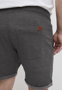 Szürke, laza fitneszes rövidnadrág, felgöngyölt szegéllyel és hátsó zsebbel. Egy barna bőr címke van feltűzve a derékszíj közelében.