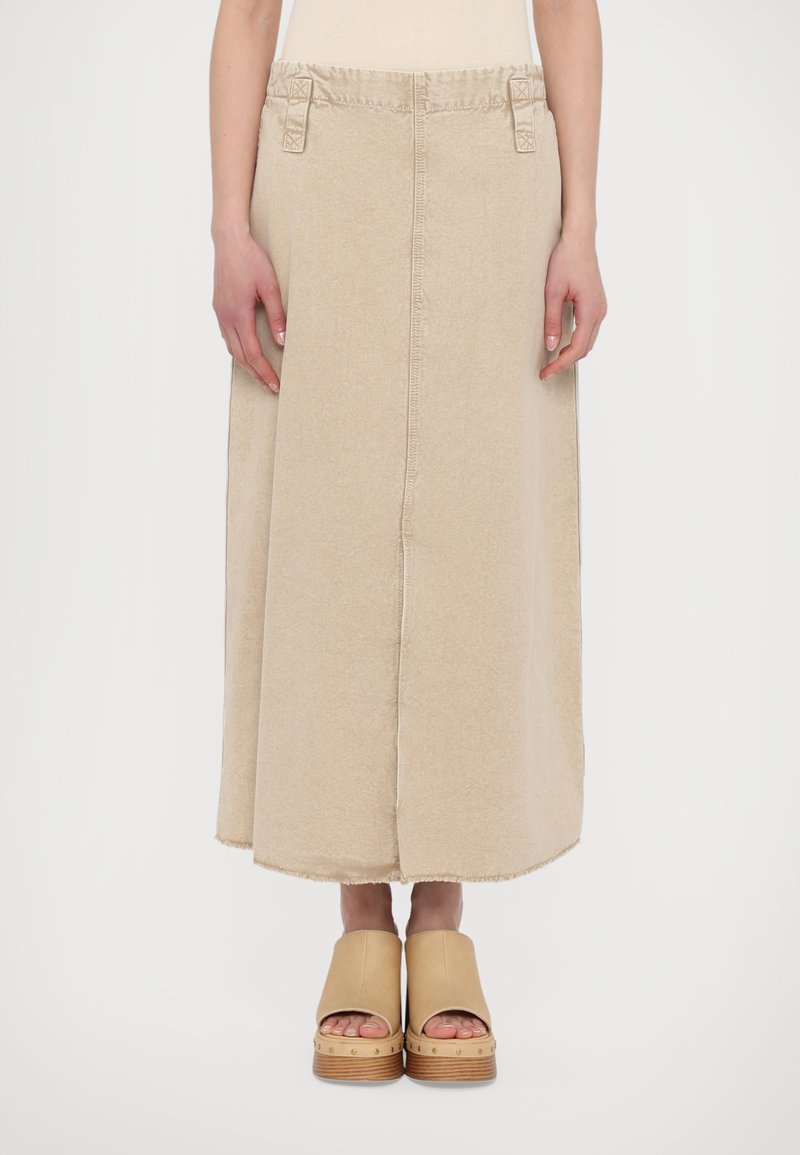 Beige lång denimkjol med rå kant, sidofickor och bältesöglor, i kombination med bruna plattformsskor med trädsulor och metallelement.