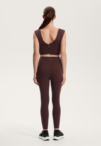 Bordo športni crop top z širokim V-izrezom, v kombinaciji z usklajenimi visokimi pajkicami, oboje iz gladkega, raztegljivega materiala, oblečeno s črnimi teniskami.