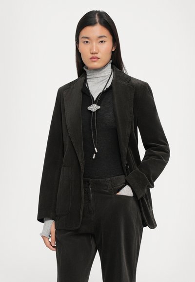 Corduroy blazer in dark green, featuring a notched lapel, front pockets, and a relaxed fit, layered over a black turtleneck.
