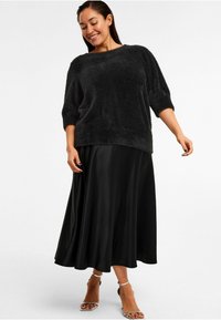 Sort fuzzy sweater med trekvartærmer, parret med en lang, flydende sort satin-nederdel og sandaler med stropper. Glat tekstur hele vejen igennem.