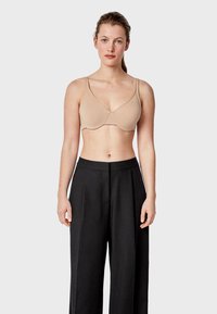 Soutien-gorge sans fil beige avec des bretelles réglables, tissu lisse et design sans coutures, porté avec un pantalon noir taille haute.