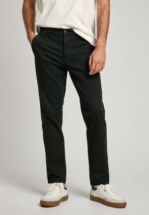 Black cotton trousers with a slim fit, featuring side pockets, a button closure, and subtle texture. Paired with white sneakers.