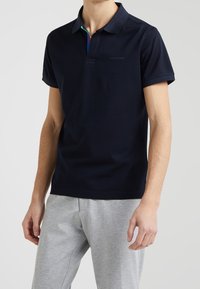 Mörkblå polo-shirt med en kontrasterande färgglad krage, korta ärmar och en logo på bröstet, tillverkad av ett mjukt bomullstyg.