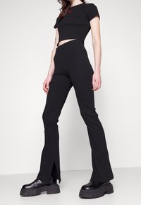 Zwarte crop top met een rood logo en hoge zwarte uitlopende broeken met zijsplitten, gecombineerd met chunky zwarte laarzen.