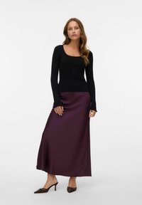 Hauts à manches longues côtelés noirs associés à une jupe maxi en satin bourgogne profond. Des talons aiguilles marron avec des accents décoratifs complètent le look.